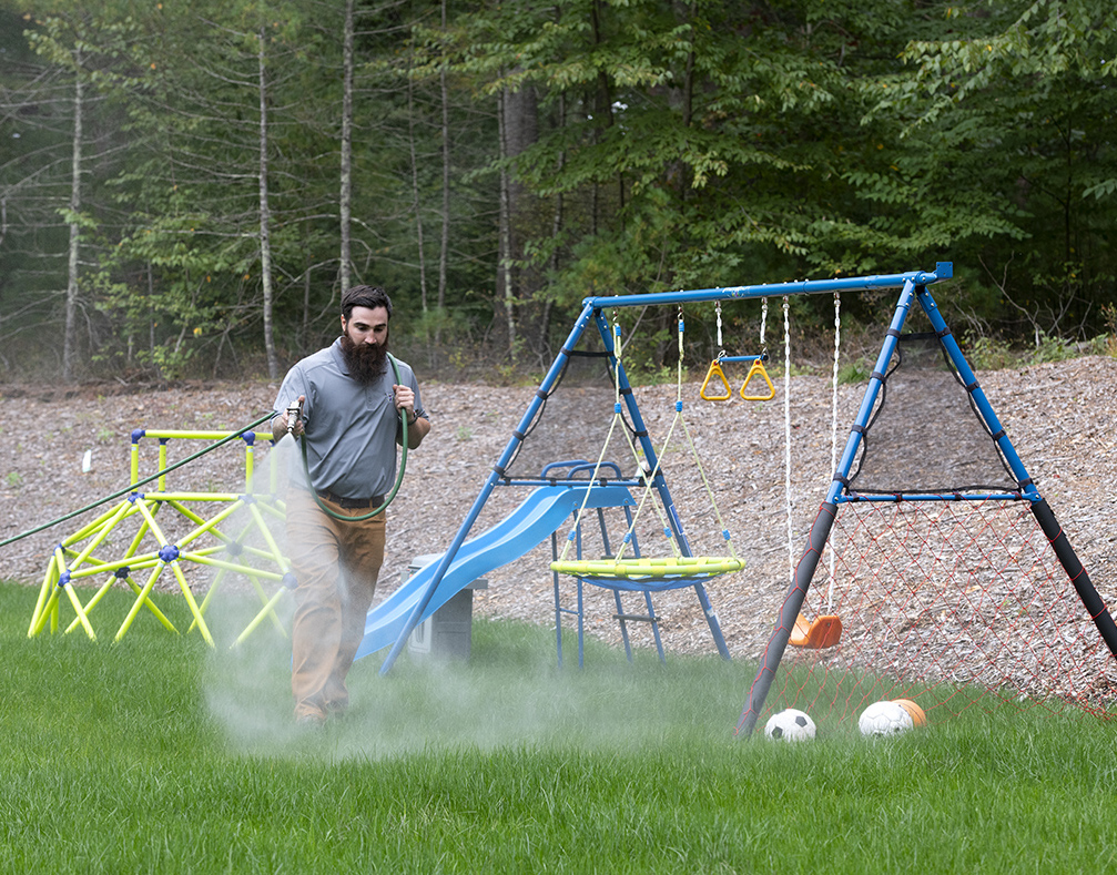 ohDEER employee with a long beard is spraying mosquito and tick control spray around a backyard playset.