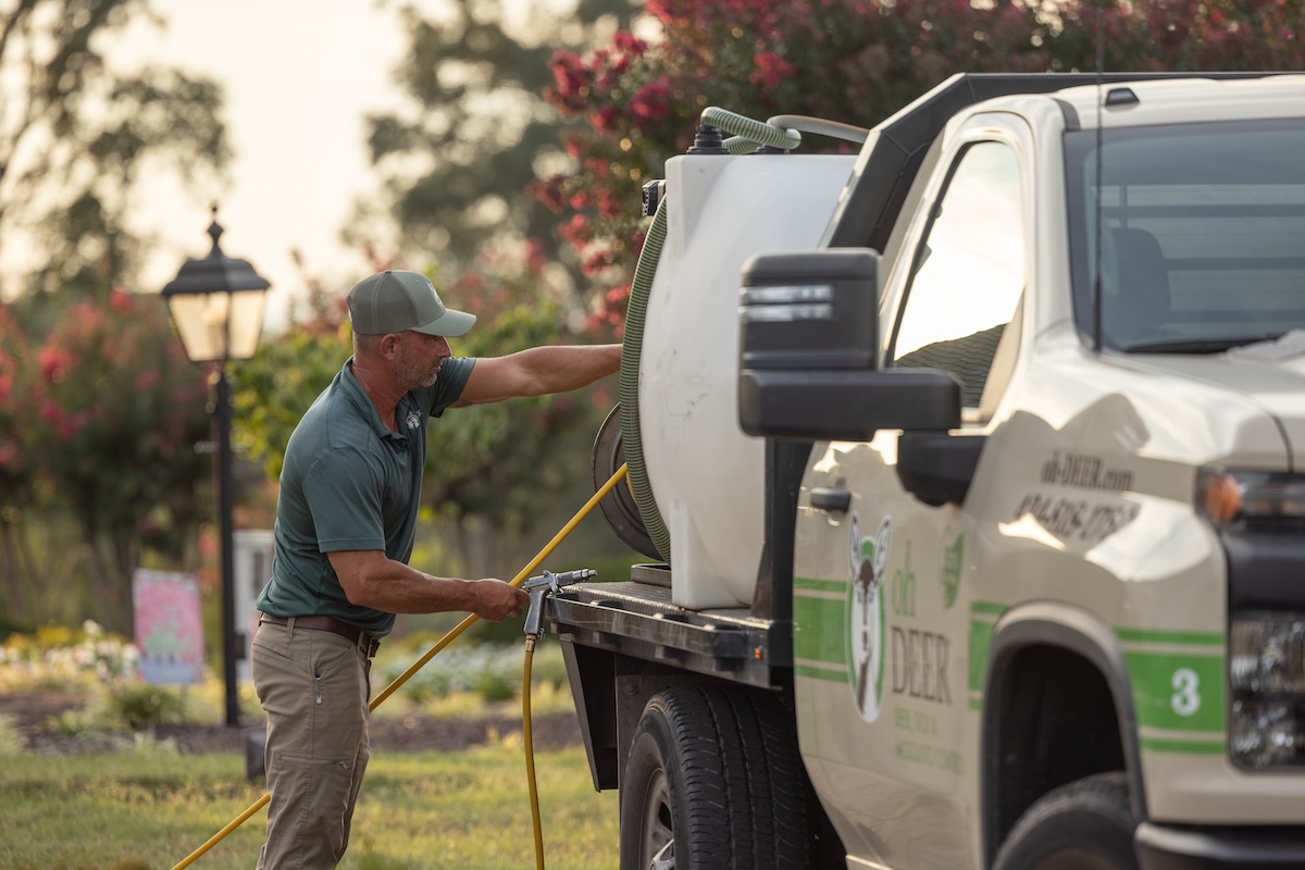 A service technician in a green uniform prepares a spray hose from a pest control truck