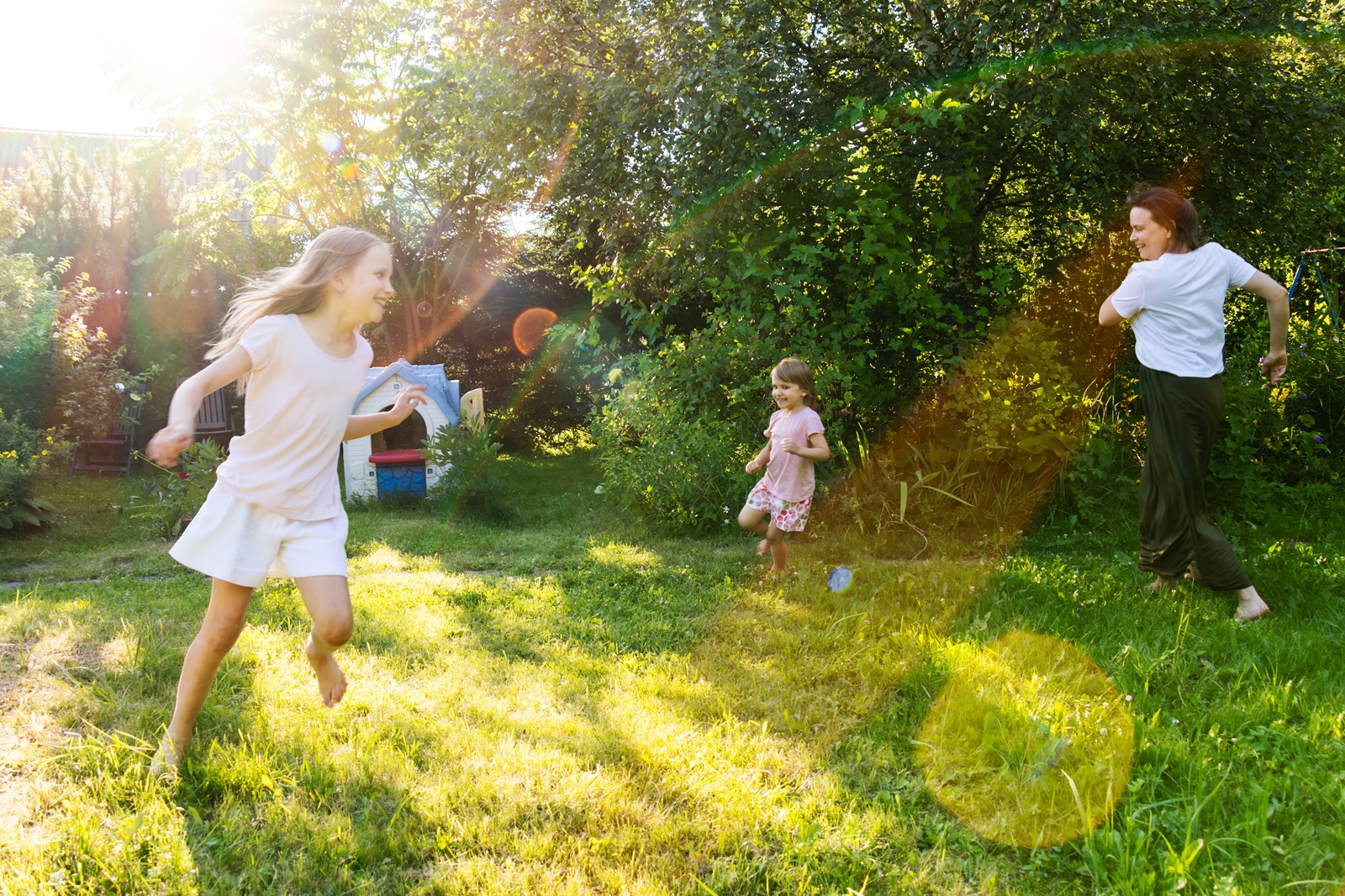 a mother and her two daughters run together in a lush green backyard