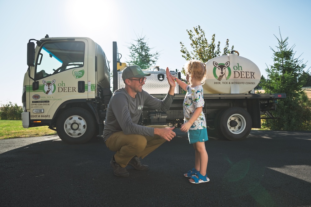 An Oh Deer pest control employee high-fives a child next to their branded truck.