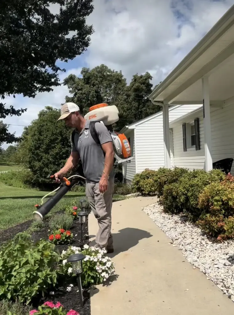 A man uses a Stihl backpack mistblower to treat a residential flower bed.