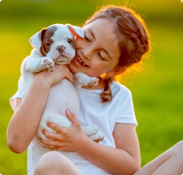 A young girl loving on a small white puppy in a green backyard that has been treated with mosquito and tick control. 