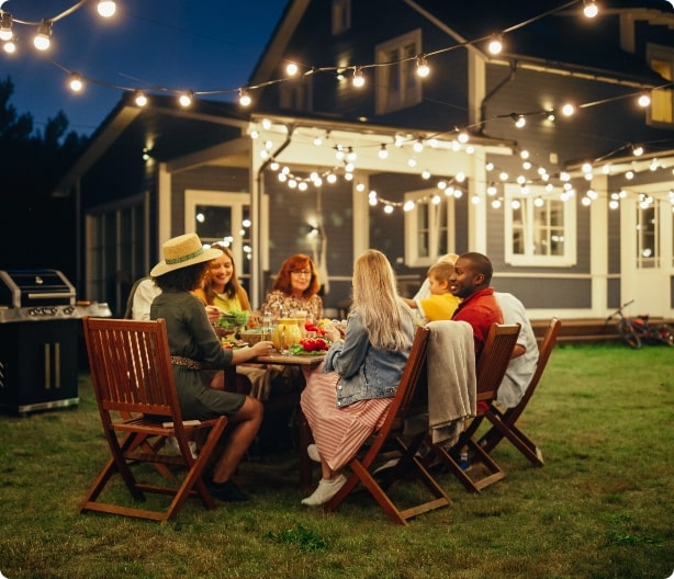 Family and friends gathered at a backyard picnic table under twinkle lights at dusk after mosquito control services were used. 