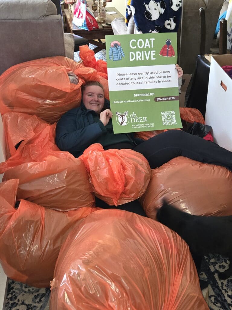 ohDEER Northwest Columbus owner laying on pile of coats collected from 2025 coat drive