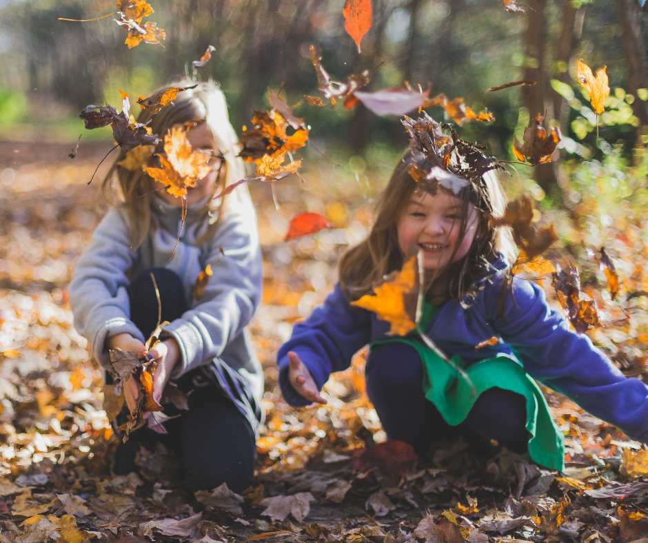 Two young girls happily play amongst a shower of autumn leaves.