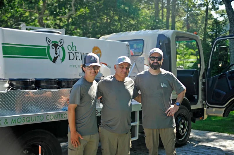 A smiling Oh Deer pest control crew stands beside their service truck.